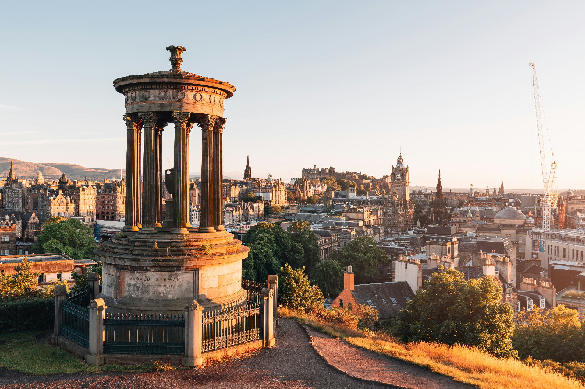 Edinburgh skyline at golden hour from Calton Hill with the Dugald Stewart Monument, Edinburgh Castle and the Balmoral clock tower
